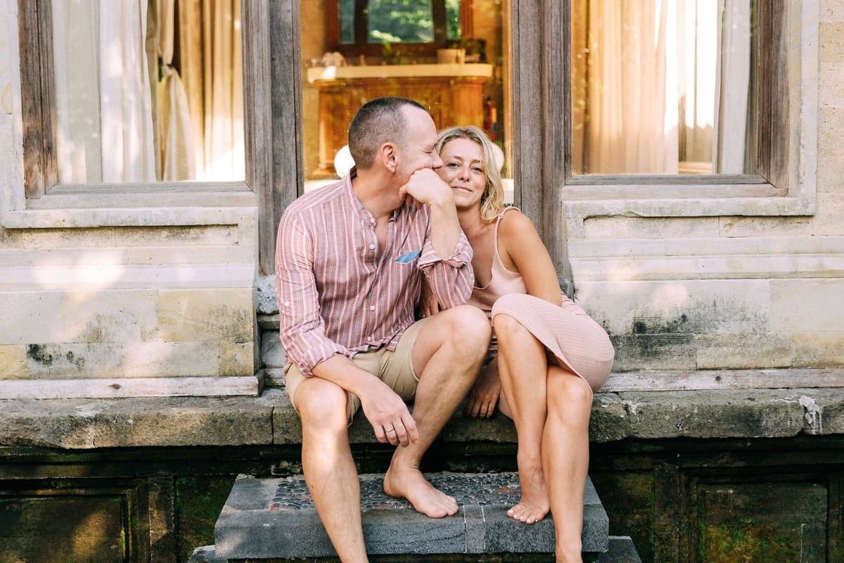 Attractive mid-40s Caucasian couple in elegant casual attire, relaxed on the steps of a luxury villa